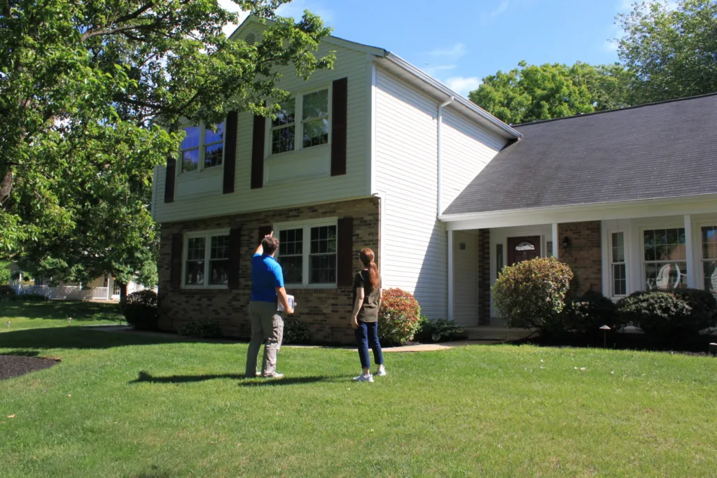 AllPro team member talking with a homeowner on the front lawn of a two-story colonial