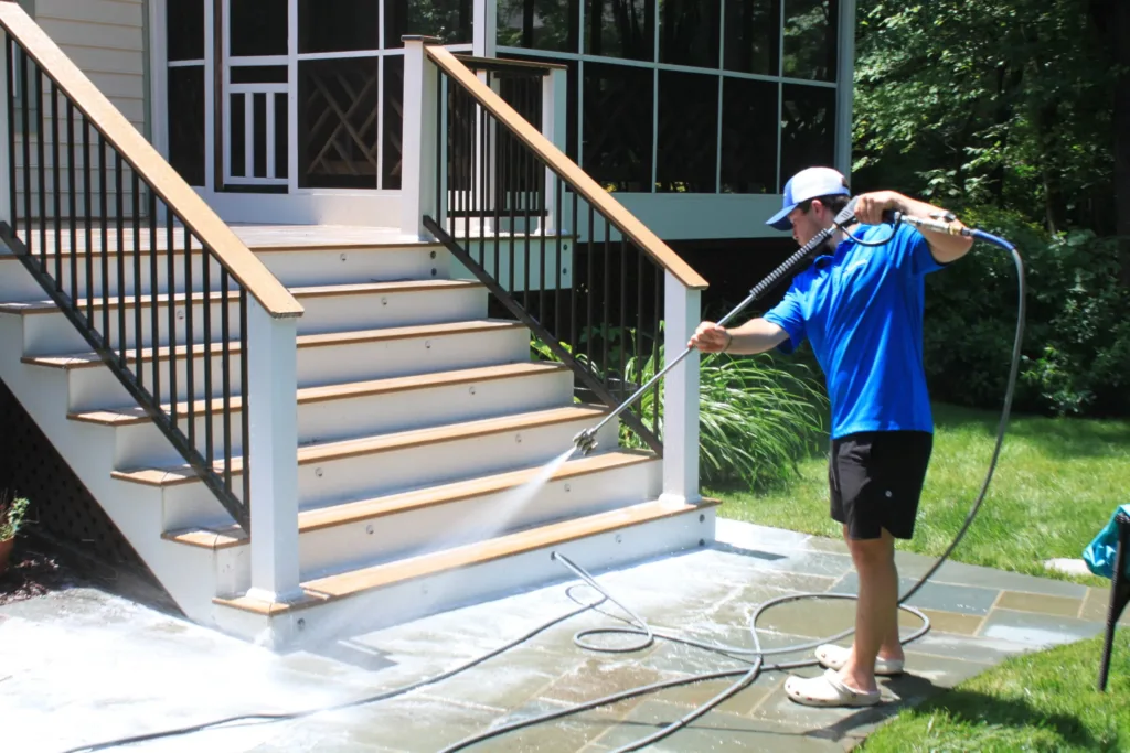AllPro technician rinsing a flagstone patio at the foot of white deck stairs