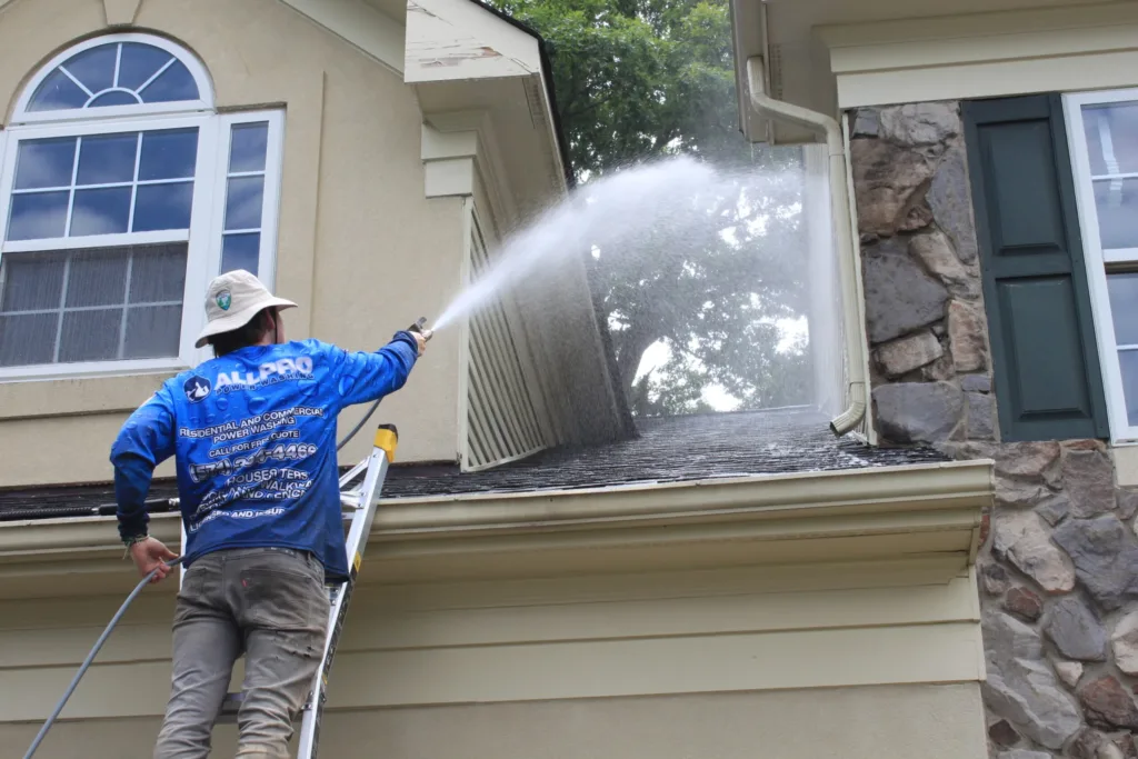 AllPro technician on a ladder spraying the siding and stonework above a front window