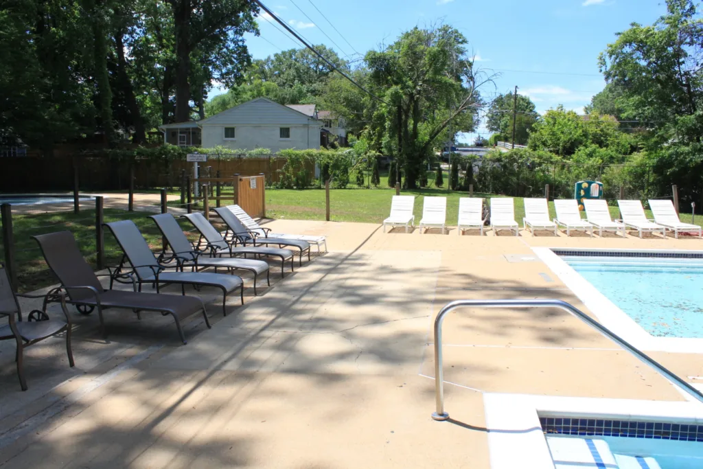 Clean concrete pool deck with lounge chairs beside a backyard pool and hot tub