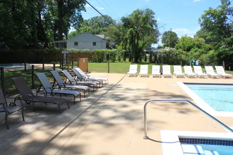 Clean concrete pool deck with lounge chairs beside a backyard pool and hot tub