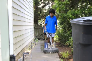 AllPro technician using a surface cleaner on a concrete walkway beside a house