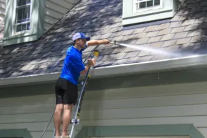 AllPro technician on a ladder cleaning the gutters and roofline of a green-sided home