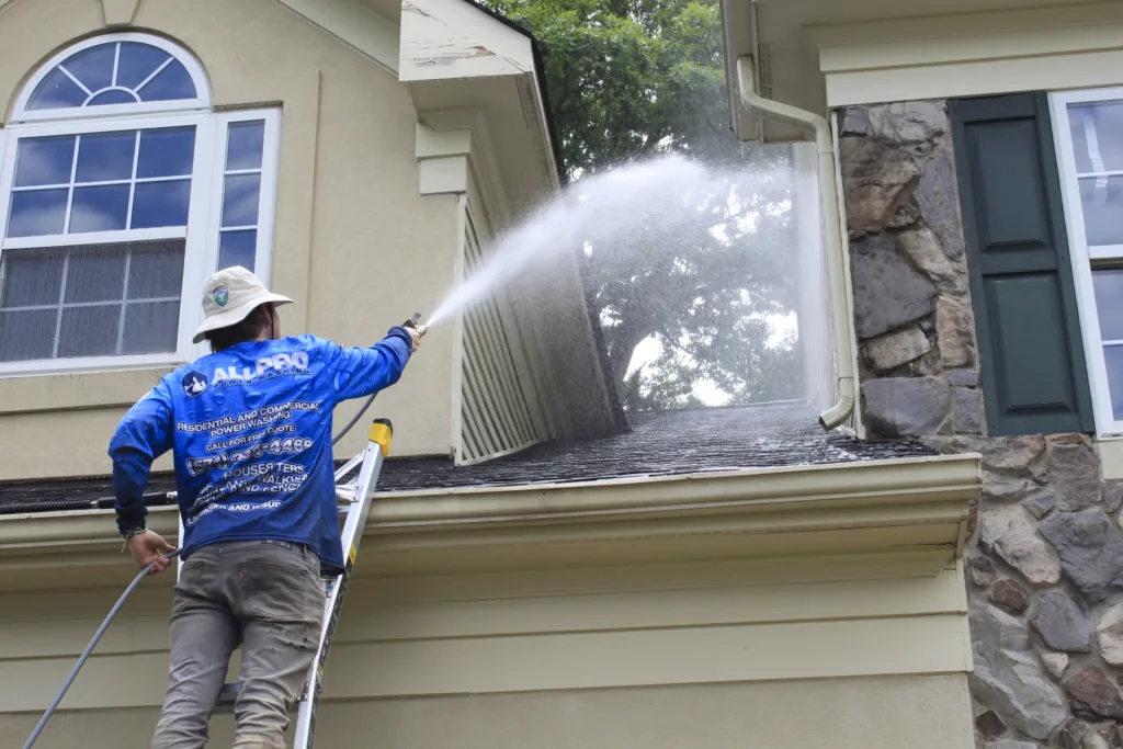 AllPro technician on a ladder spraying the siding and stonework above a front window