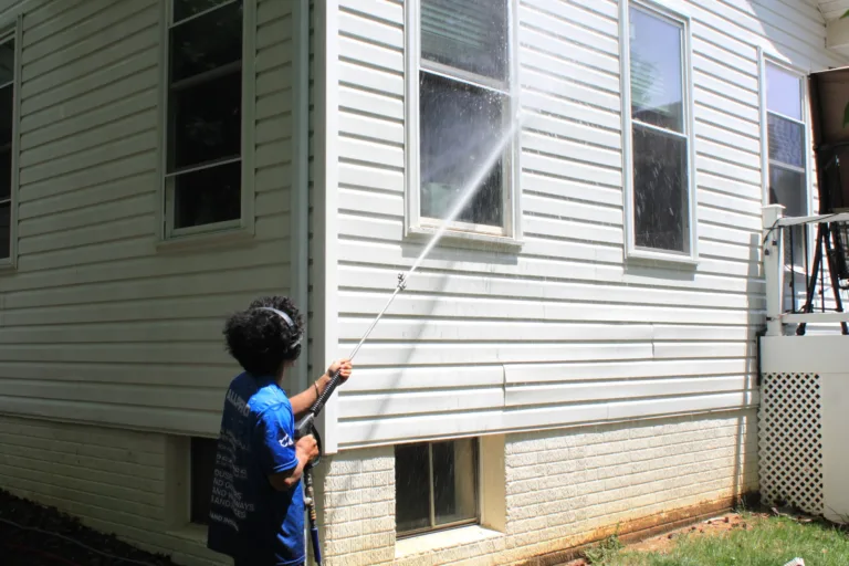 AllPro technician washing white vinyl siding on a home